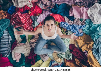 High angle above view photo of stressed helpless lady stay home spring cleaning household sit many clothes stack floor pick select outfit nothing to wear concept all stuff dirty indoors