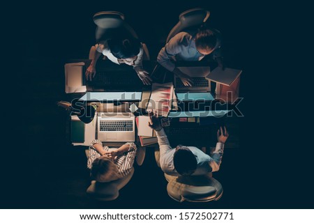 High angle above view photo of hard-working four busy business men women working overtime looking computer screen talking about startup lamp light dark office indoors