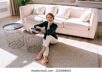 High Angle Of Adult Barefoot Woman Leaning On Hand And Sitting With Crossed Legs Near Laptop While Working In Stylish Living Room