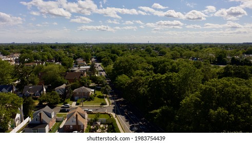 A High Angle, Aerial View Over A Suburban Neighborhood In Queens, NY. It Is A Sunny Day With Green Trees Everywhere.