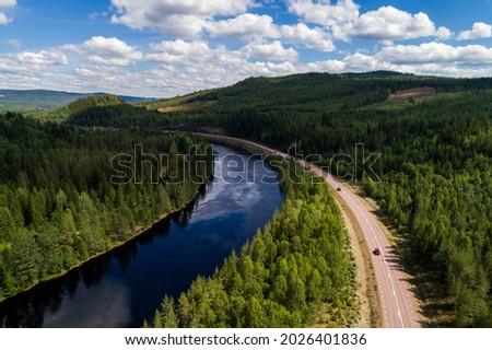High angle aerial view of river and road running through forest and mountainous landscape in northern Sweden