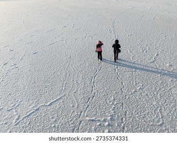 High angle aerial view of two people walking on a vast frozen lake covered in white snow and ice textures.