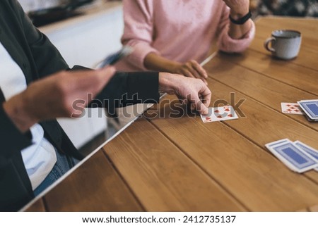 High angle of anonymous senior women in casual clothes sitting at wooden table playing board game having competition while drinking hot beverage