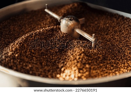 High angle of aromatic freshly roasted coffee beans in large cooling tray of roasting machine at factory