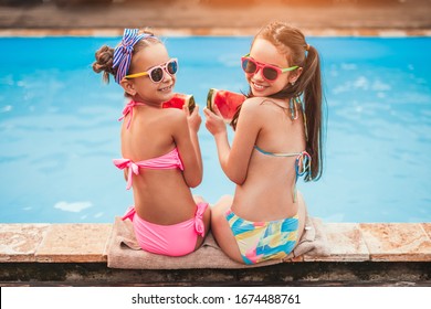 High angle back view of happy friends in sunglasses and colorful swimsuits with slices of fresh tasty watermelon looking, over shoulder at camera and smiling while sitting on poolside pool - Powered by Shutterstock