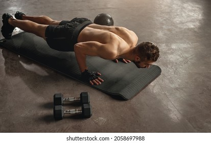 High angle back view of muscular sportsman with naked torso pushing up during functional training on mat in gymnasium
