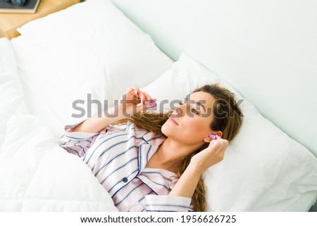 High angle of a beautiful woman ready to fall asleep while putting earplugs to avoid the noise and have a good night sleep