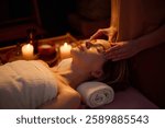 High angle of blonde woman lying on towel roll and getting facial massage by professional masseuse, room filling with aroma scent slowly