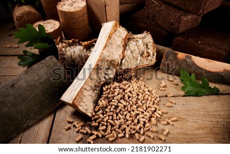 High angle of chopped birch and oak firewood scattered on wooden table near fuel pellets and cylindrical and square biomass briquettes