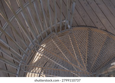High angle close up shot looking down the entry point of an outdoor spiral metal staircase with railings and wooden deck floor. Architectural details showcasing industrial patterns and lines