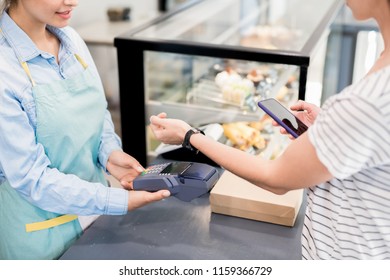 High angle close up of unrecognizable woman paying via smart watch  and smartphone in local bakery, copy space - Powered by Shutterstock