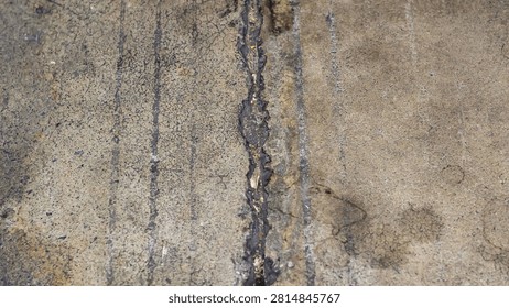 High angle close up view of a damaged weathered concrete road floor showing a vertical crack filled with dark asphalt sealant and grooved lines background
