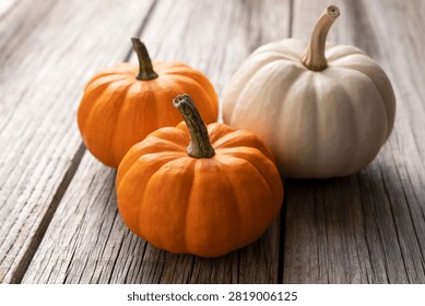 High angle close up view of two small orange pumpkins and one white pumpkin arranged on a rustic weathered wooden surface.
