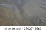 High angle close up view of wet sand beach shore displaying unique organic patterns and lines shaped by receding water waves