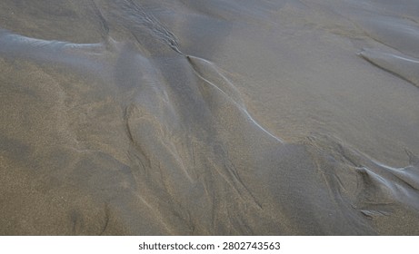 High angle close up view of wet sand beach shore displaying unique organic patterns and lines shaped by receding water waves