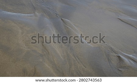 High angle close up view of wet sand beach shore displaying unique organic patterns and lines shaped by receding water waves