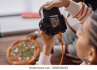 High angle closeup of female photographer holding camera during food photography set taking pictures of fresh rustic pizza on wooden table copy space - Powered by Shutterstock