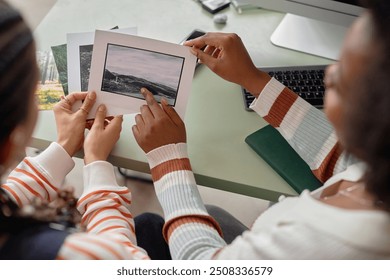 High angle closeup of two African American two women collaborating on creative project and holding photo prints with nature landscapes - Powered by Shutterstock