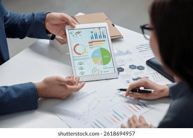 High angle closeup of two unrecognizable colleagues discussing data statistics on tablet screen during meeting in office copy space