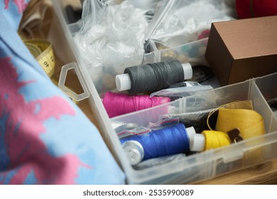 High angle of container with several multi-color thread bobbins, rolled measuring tape, brown box and cellophane sacks - Powered by Shutterstock