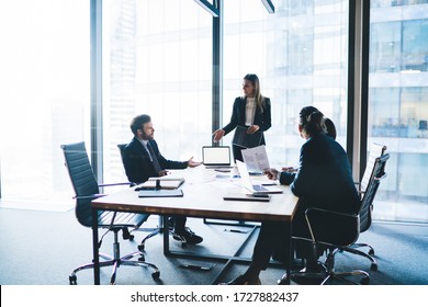 High angle of content female entrepreneur in elegant clothes explaining business strategy to board of directors while standing near table during meeting