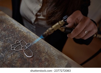 High angle of crop anonymous craftswoman making creative metal jewellery accessory with gas burner in workroom - Powered by Shutterstock