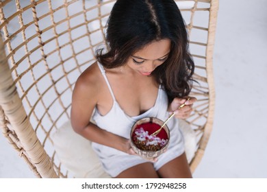 High Angle Of Crop Focused Ethnic Young Tanned Female In Casual Clothes Eating Fresh Healthy Vegan Bowl With Berries And Coconut Flakes