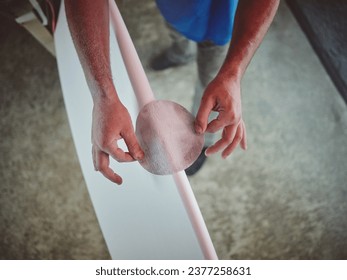 High angle of crop tattooed anonymous male worker sanding surfboard while working in craft workroom - Powered by Shutterstock