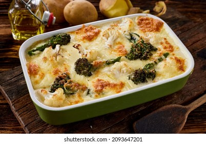 High angle of delicious homemade broccoli and cauliflower gratin prepared in ceramic pan with cheese and veggies and served on wooden cutting board in kitchen