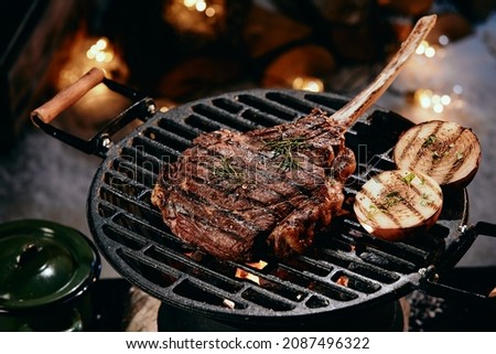 High angle of delicious hot Tomahawk steak and halves of onion preparing on grill rack in winter night