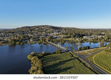 High angle drone shot captures a bridge over calm water connecting farmland to town.