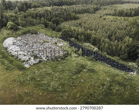 A high angle drone shot capturing environmental pollution and degradation caused by unregulated dumping. Huge piles of mixed rubbish and scrap rubber tires contrast with the surrounding natural woodland scenery.