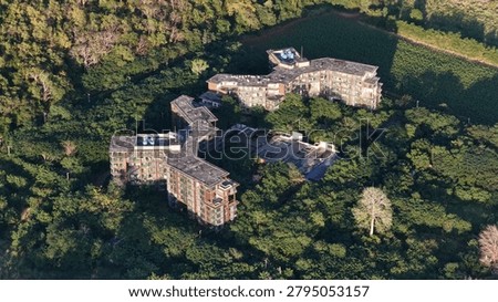High angle drone shot of decaying hotel structures being reclaimed by dense tropical forest vegetation.