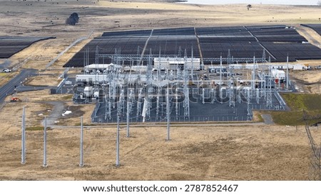 High angle drone shot of a large solar panel array and electrical power substation.