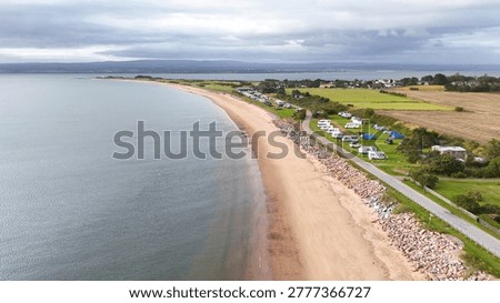 High angle drone shot of a sandy shoreline, caravan park, and calm coastal waters.