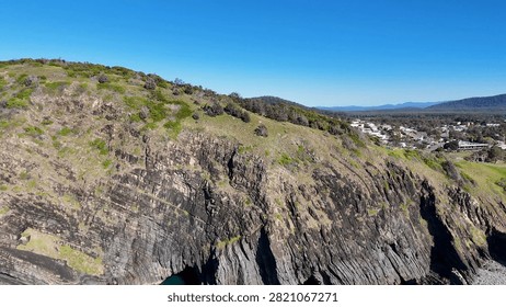 High angle drone shot of steep rocky cliffs and coastal town at Crescent Head.