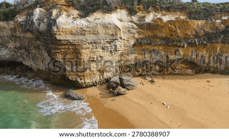 High angle drone shot of turquoise waves washing onto a sandy beach beneath towering cliffs.