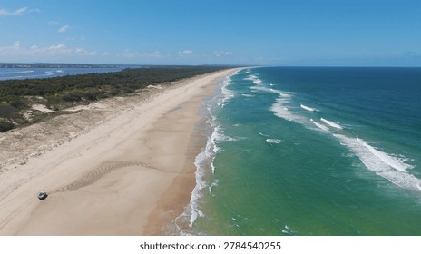 High angle drone shot of waves crashing on a sandy beach with a vehicle.