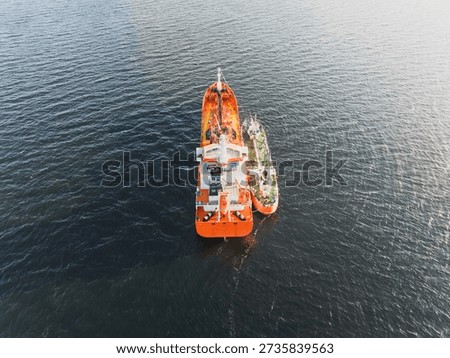 High angle drone view of a large orange tanker being refueled by a bunker barge ship in the open sea.