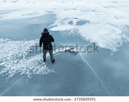 High angle drone view of a man in winter clothes standing on the cracked frozen surface of the Baltic Sea.