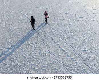 High angle drone view of two people walking on the frozen Baltic Sea surface in Estonia during cold winter day.