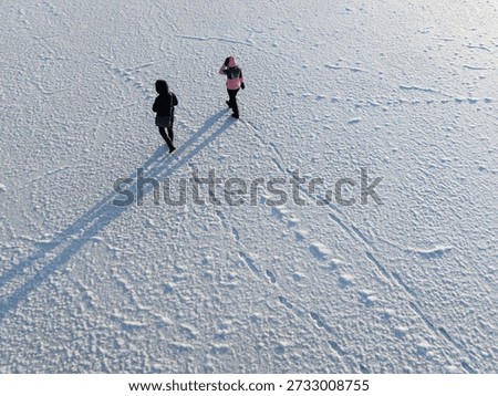 High angle drone view of two people walking on the frozen Baltic Sea surface in Estonia during cold winter day.