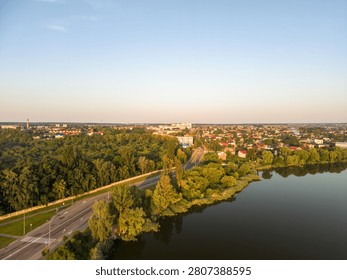 High angle drone viewpoint captures a green lakeside residential neighborhood of Vinnytsia with an asphalt road under a clear morning sky.