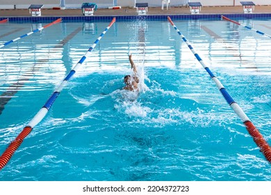 High angle front view of a Caucasian male swimmer at swimming pool, wearing a swimming cap and goggles splashing, swimming backstroke - Powered by Shutterstock