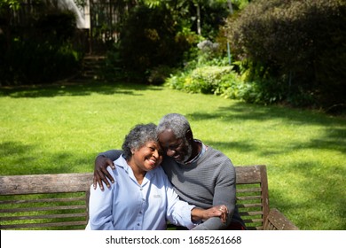 High angle front view of senior African American couple in the garden, sitting on a bench, embracing and talking. Family enjoying time at home, lifestyle concept