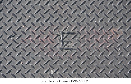 High angle full frame close-up view of a steel plate cover on a sidewalk with the letter E welded on
