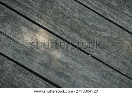 High angle full frame shot of rustic grey wooden boards arranged diagonally, showing textured grain patterns and weathered surface details illuminated by a soft patch of natural sunlight.