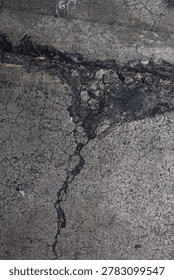 High angle full frame view of a badly damaged grey asphalt road showing a deep pothole filled with broken bitumen pieces and surrounded by a dense network of alligator cracking