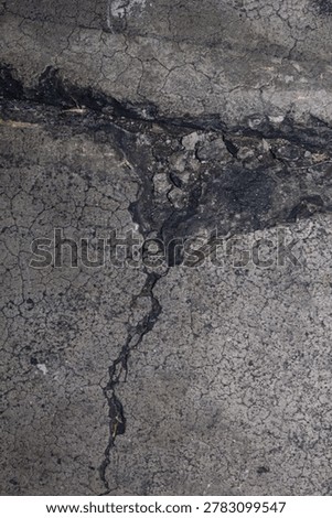 High angle full frame view of a badly damaged grey asphalt road showing a deep pothole filled with broken bitumen pieces and surrounded by a dense network of alligator cracking