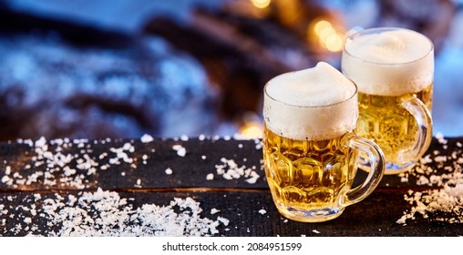 High Angle Of Glass Mugs Of Cold Beer With Foam Served On Wooden Table With Snow In Winter Garden At Night